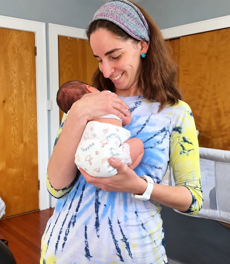 Smiling woman in a tie-dye top holding a newborn against her chest